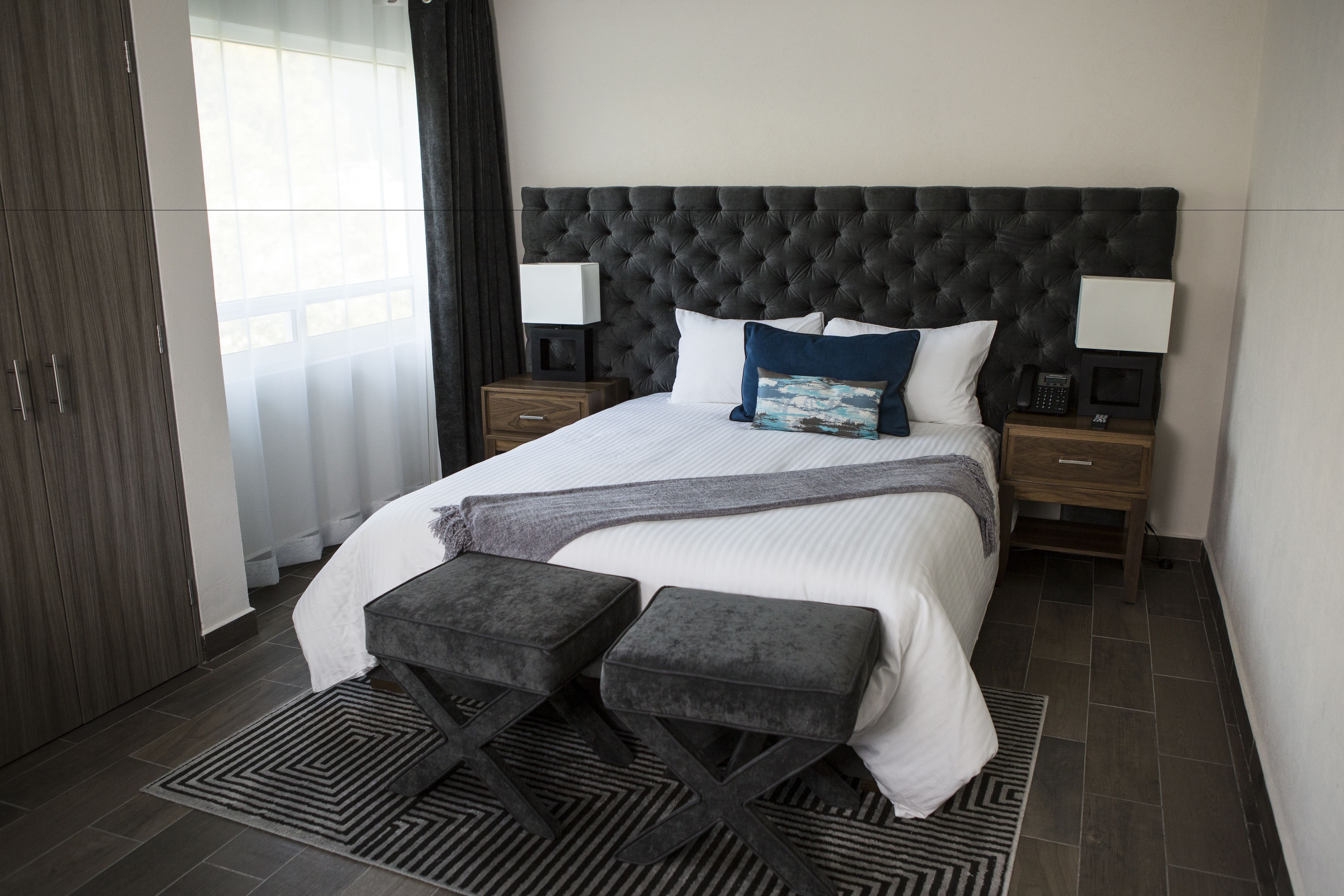A modern bedroom with a tufted headboard, a large bed with white linens, two bedside tables with lamps, and a patterned rug.