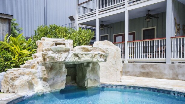 Una piscina con una cascata artificiale rocciosa, circondata da un balcone bianco con ringhiere.