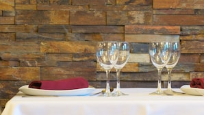 Een tafel gedekt met twee wijnglazen en gevouwen servetten op een witte tafelkleed, met een stenen muur op de achtergrond.