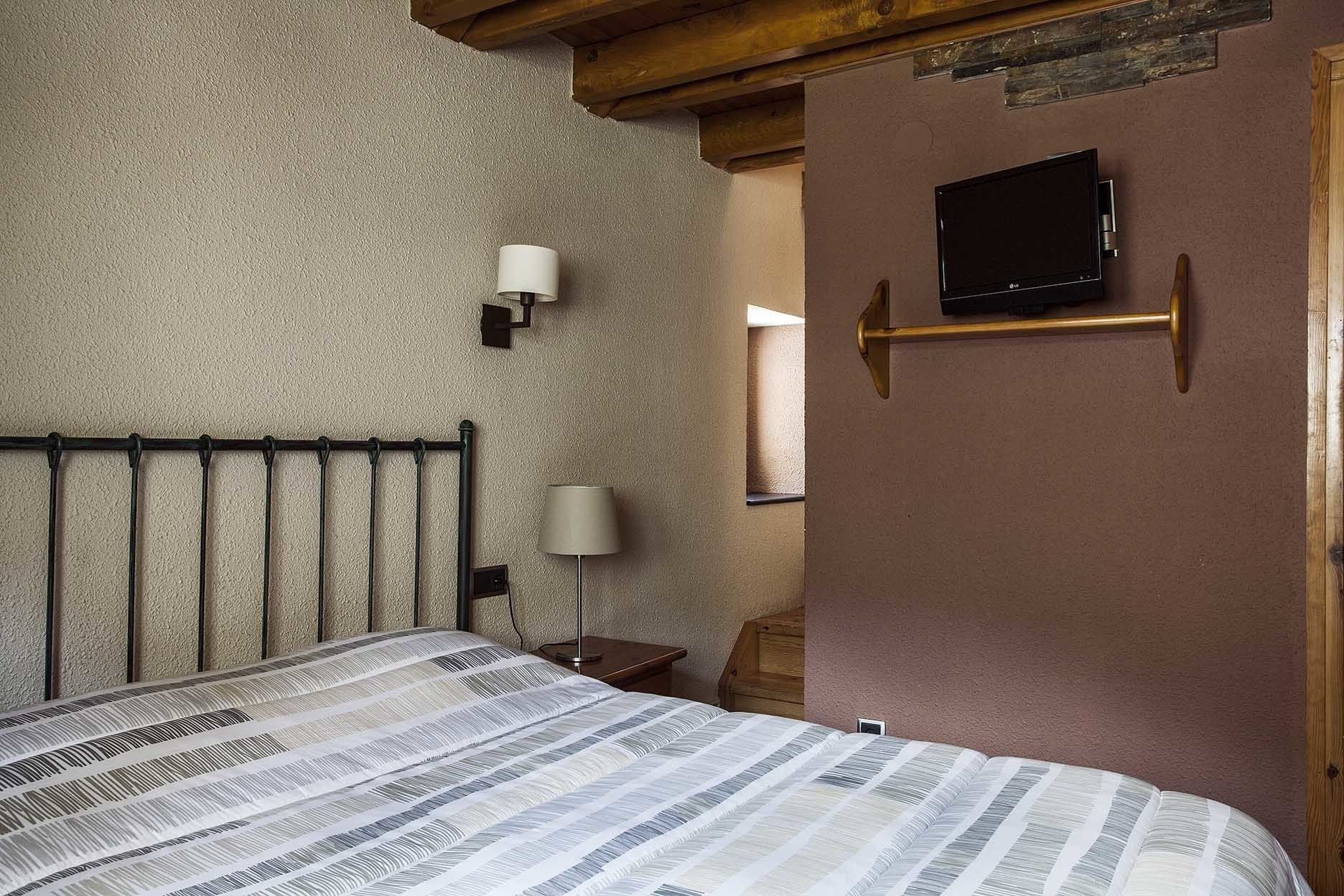 Un dormitorio con cama, televisor montado en la pared y lámpara en la mesita de noche.