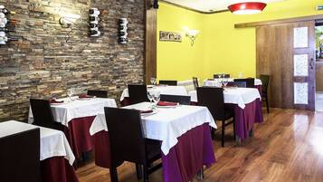 Un restaurante con paredes de piedra, suelos de madera y mesas dispuestas con manteles blancos y servilletas rojas.