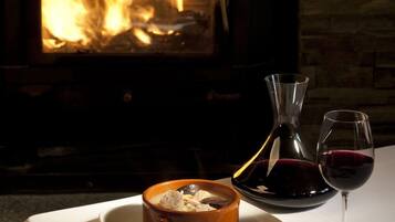 Una mesa con un bol de comida, una copa de vino y un botellero, con un hogar encendido de fondo.