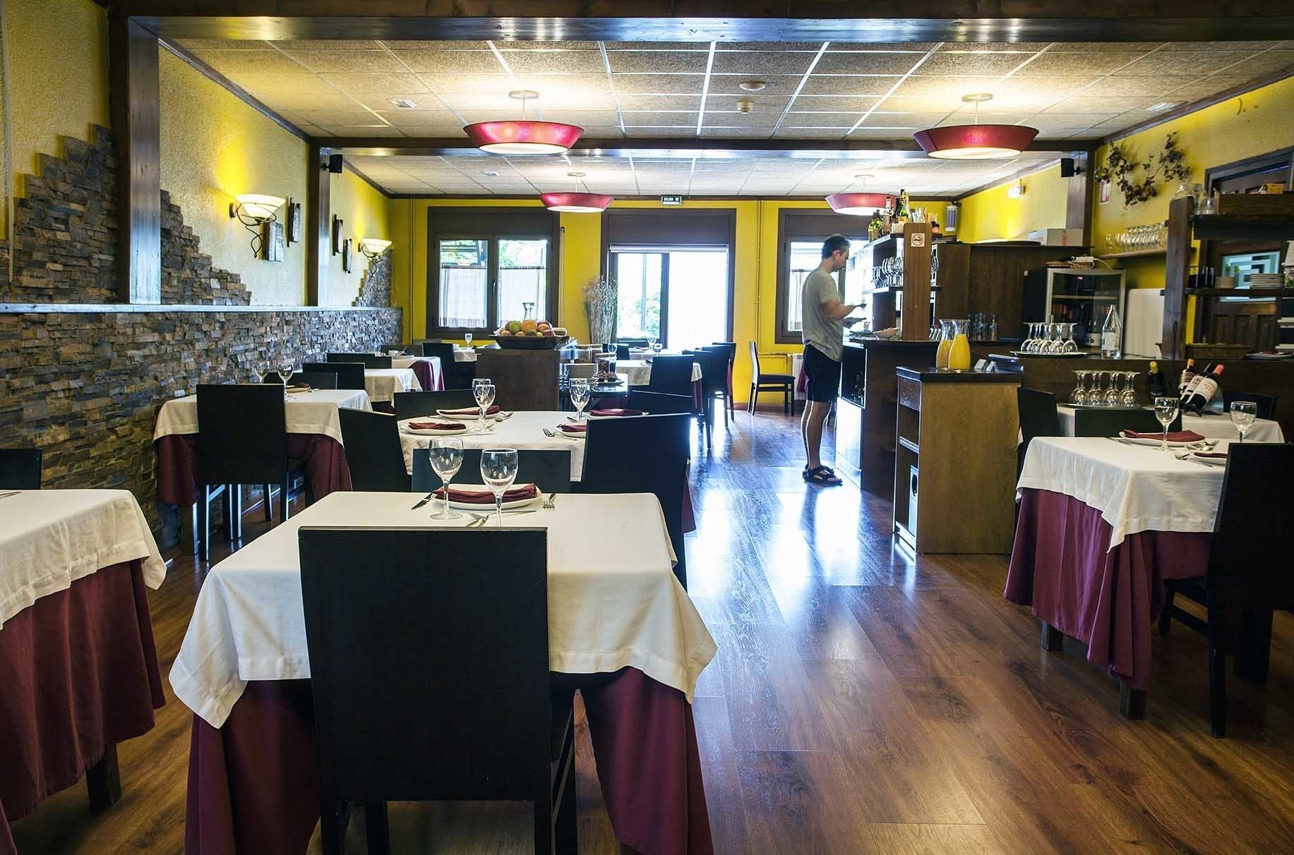 Een restaurantinterieur met meerdere eettafels, een bar en een stenen muur.