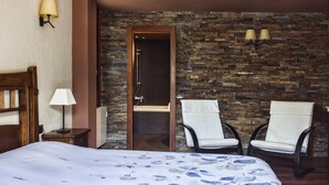 Een hotelkamer met een groot bed, twee stoelen, een houten deur en een stenen muur.