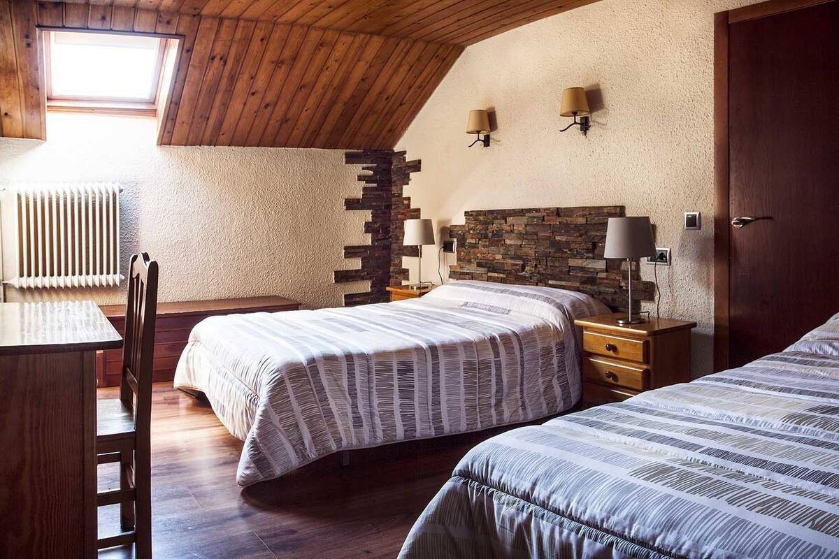 Un dormitorio con dos camas, un escritorio de madera, una silla, un radiador y una pared de piedra.