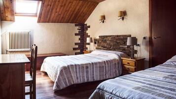 Une chambre avec deux lits, un bureau en bois, une chaise, un radiateur et un mur en pierre.