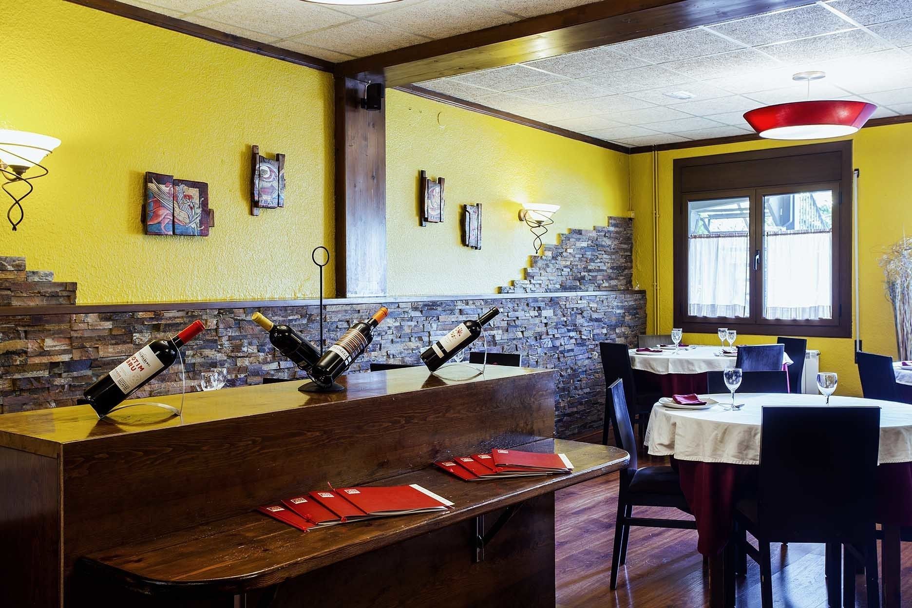 Interior de restaurante com balcão de madeira, paredes amarelas e parede de pedra ao fundo.