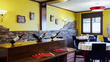 Interior de restaurante com balcão de madeira, paredes amarelas e parede de pedra ao fundo.