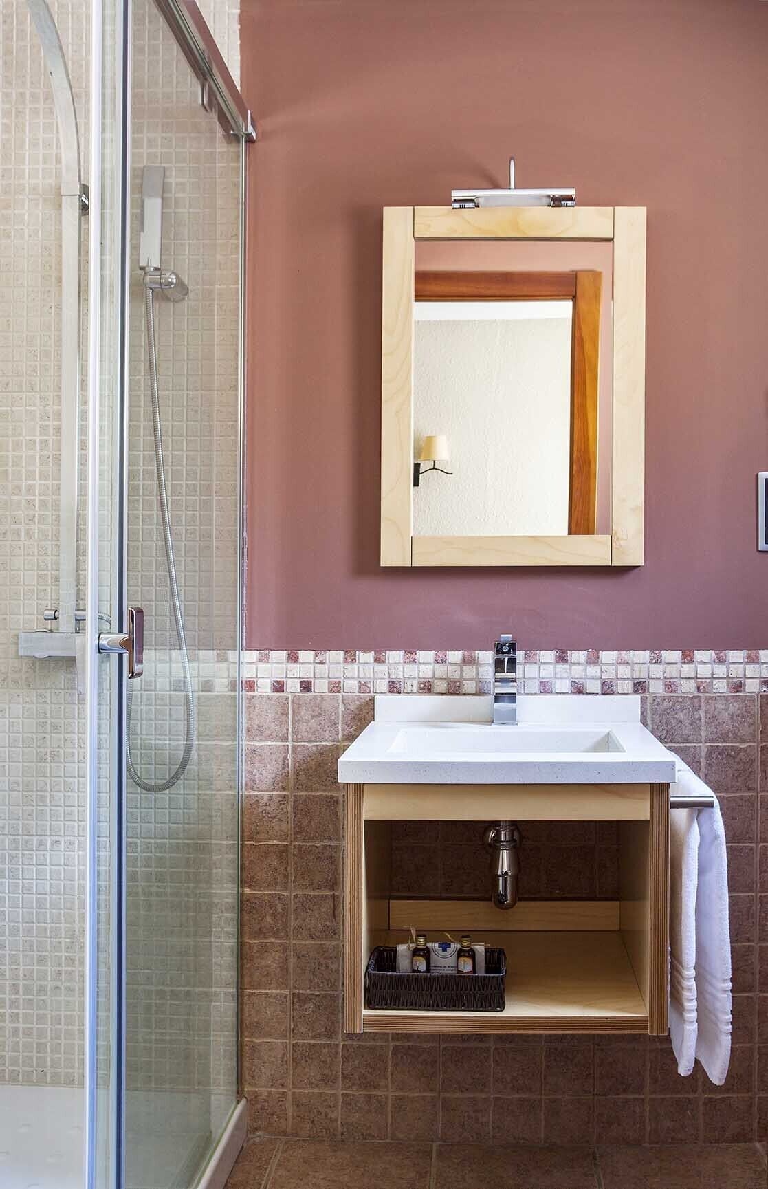 Un baño con cabina de ducha de vidrio, un lavamanos blanco con un gabinete de madera debajo y un espejo encima.