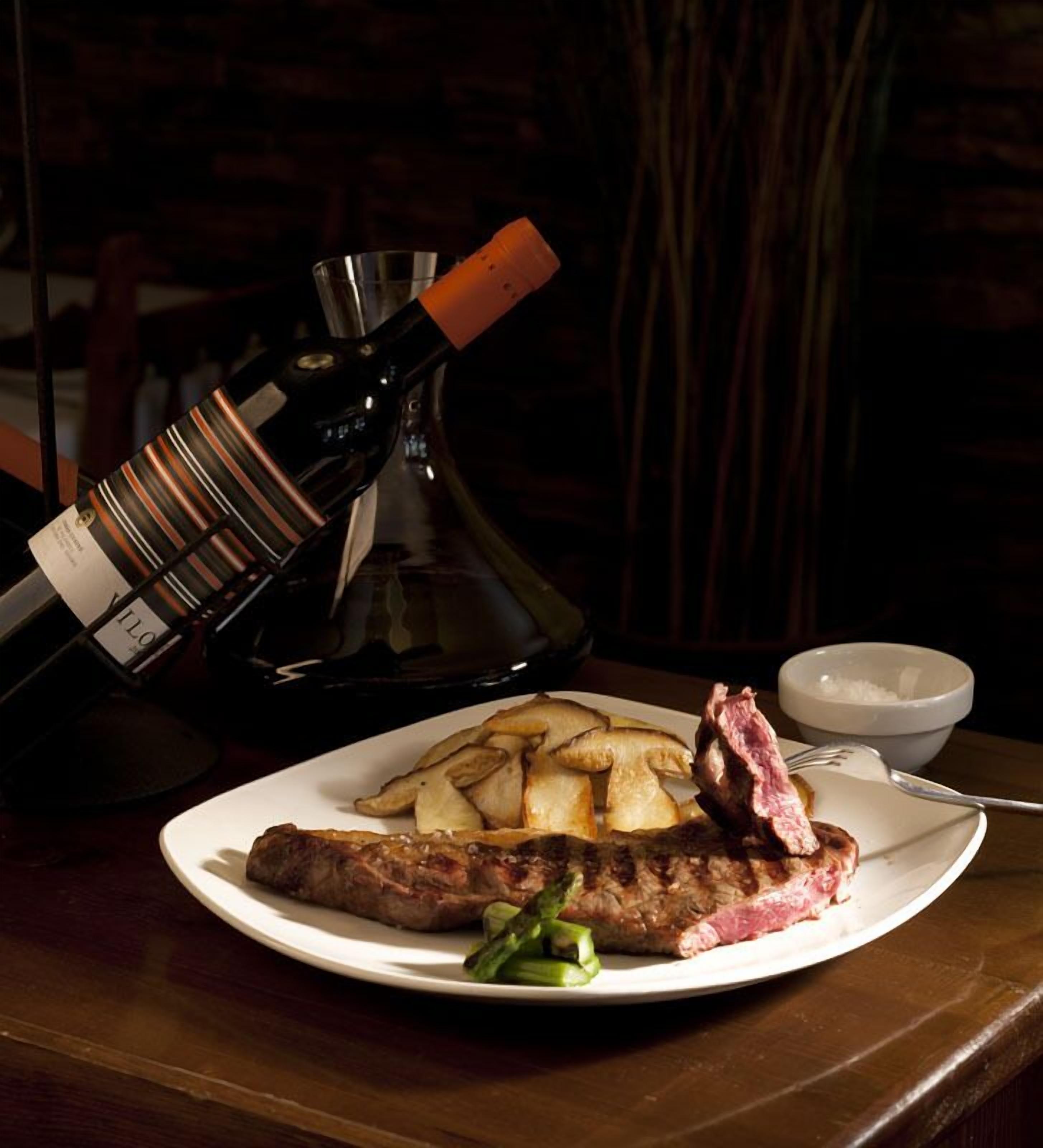 A plate with steak and fries, a bottle of wine, and a bowl of salt on a wooden table.