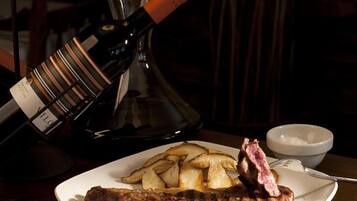 A plate with steak and fries, a bottle of wine, and a bowl of salt on a wooden table.