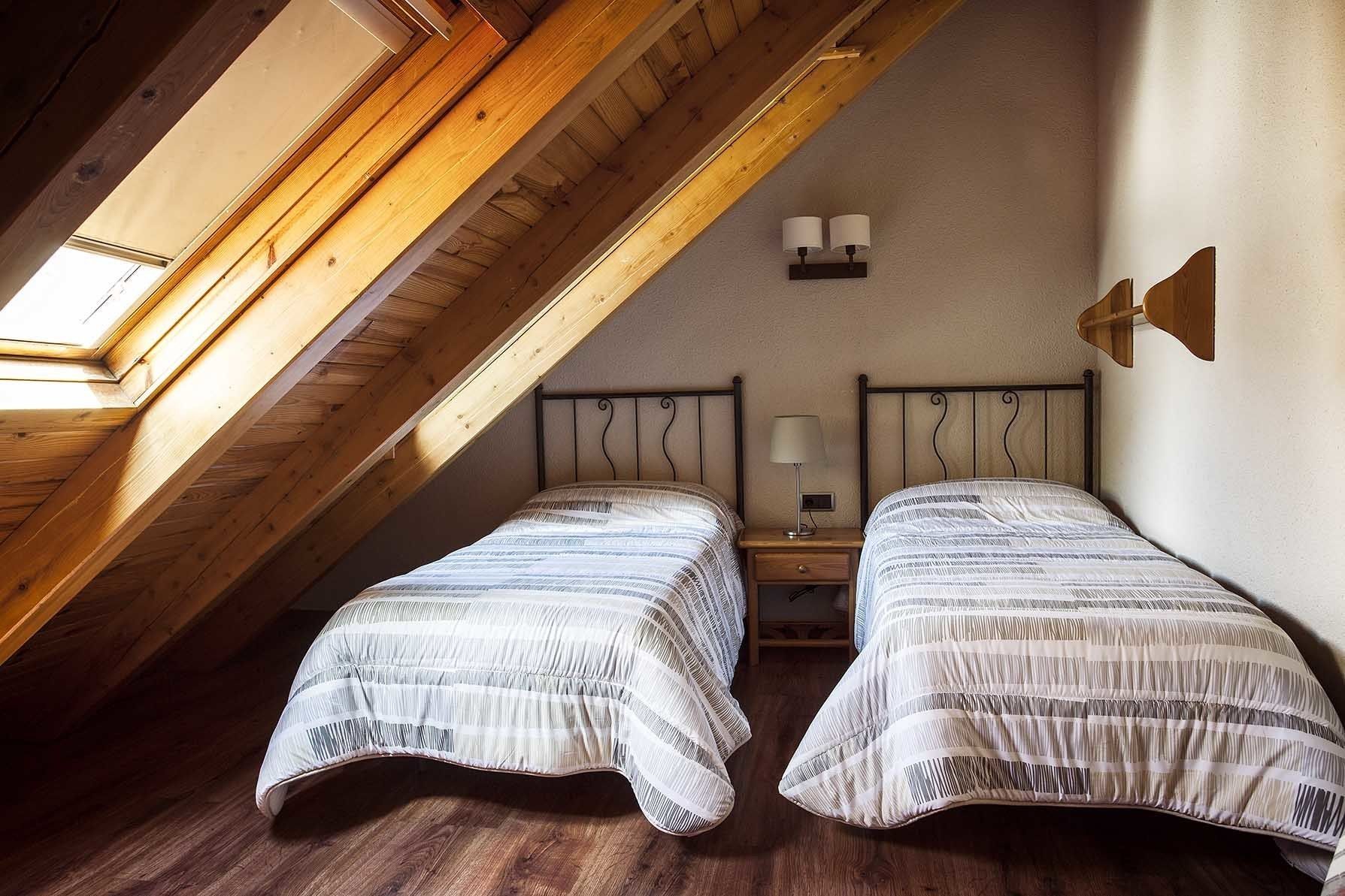 Une chambre avec deux lits, des poutres en bois, un plafond en pente et un puits de lumière.