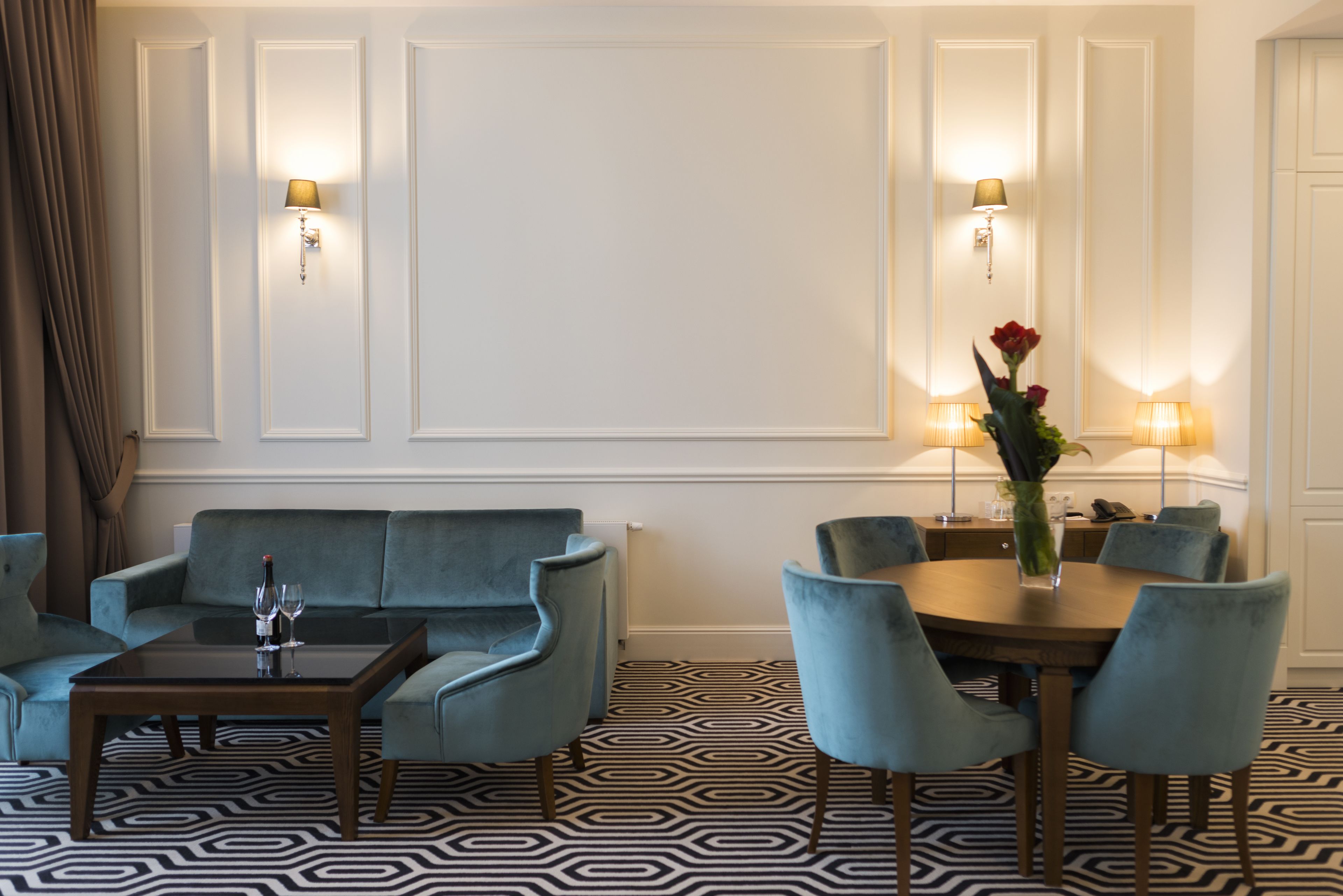 Hotelkamer met een bank, een eettafel met stoelen, een kamer met een patroon en wandlampen.