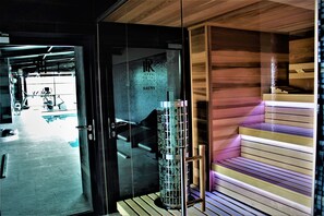 A sauna area with a glass door, a wooden bench, and a metal structure. - Hotel Royal & Spa (Bialystok)