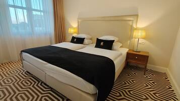 Una habitación de hotel con una cama grande, dos mesitas de noche con lámparas, una alfombra estampada y una ventana con cortinas.