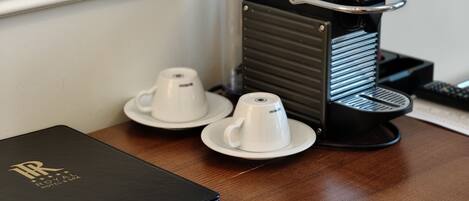 A coffee machine with two white cups on a wooden table, a black folder, and a remote control.