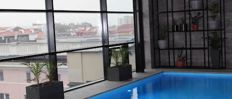 An indoor swimming pool with a view of buildings through large windows.