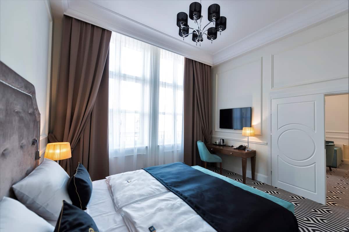 A hotel room with a bed, a desk, a chair, a TV, and a door.