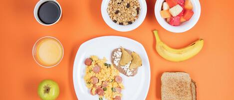 A breakfast plate with scrambled eggs, sausage, and beans, accompanied by a banana, toast, a glass of orange juice, a bowl of cereal, a bowl of fruit, and a cup of coffee.