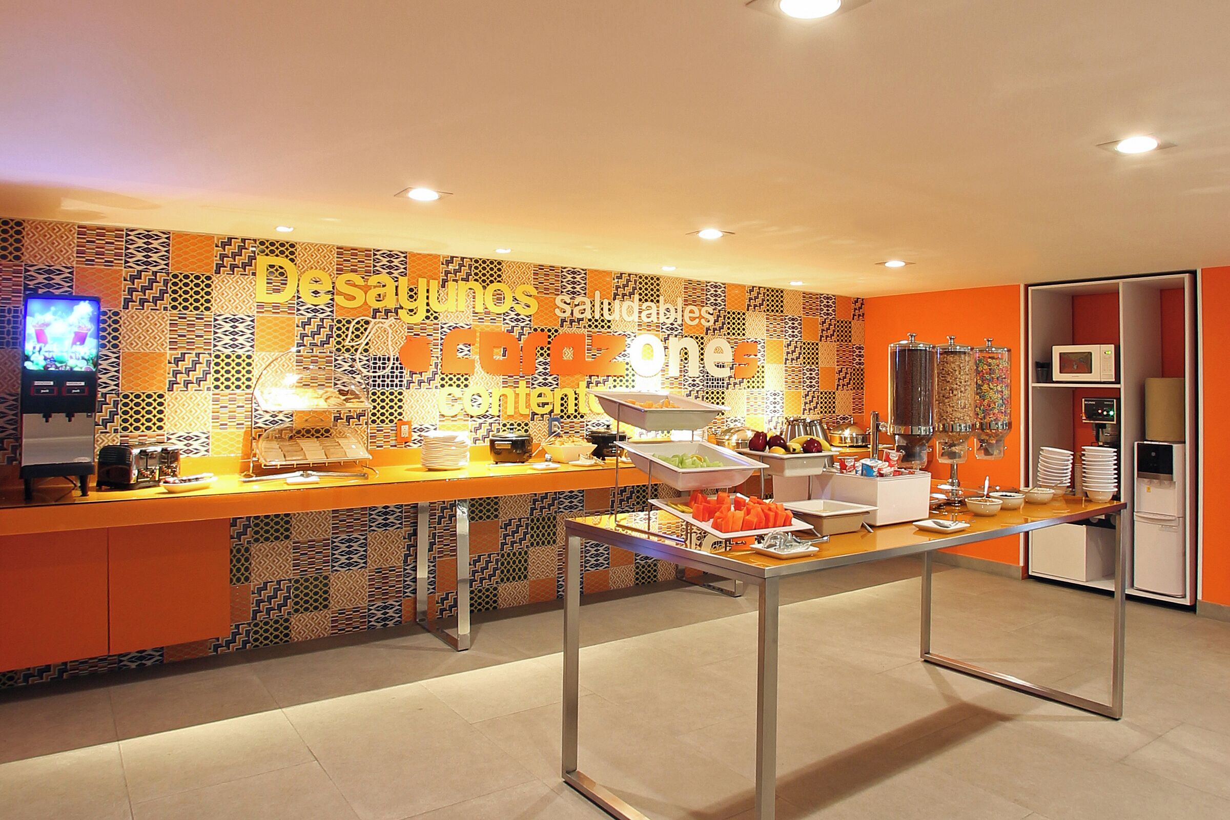 Un área de bufé con una pared de azulejos coloridos, una mesa de bufé con diferentes alimentos y un microondas al fondo.