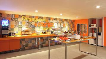 Un área de bufé con una pared de azulejos coloridos, una mesa de bufé con diferentes alimentos y un microondas al fondo.