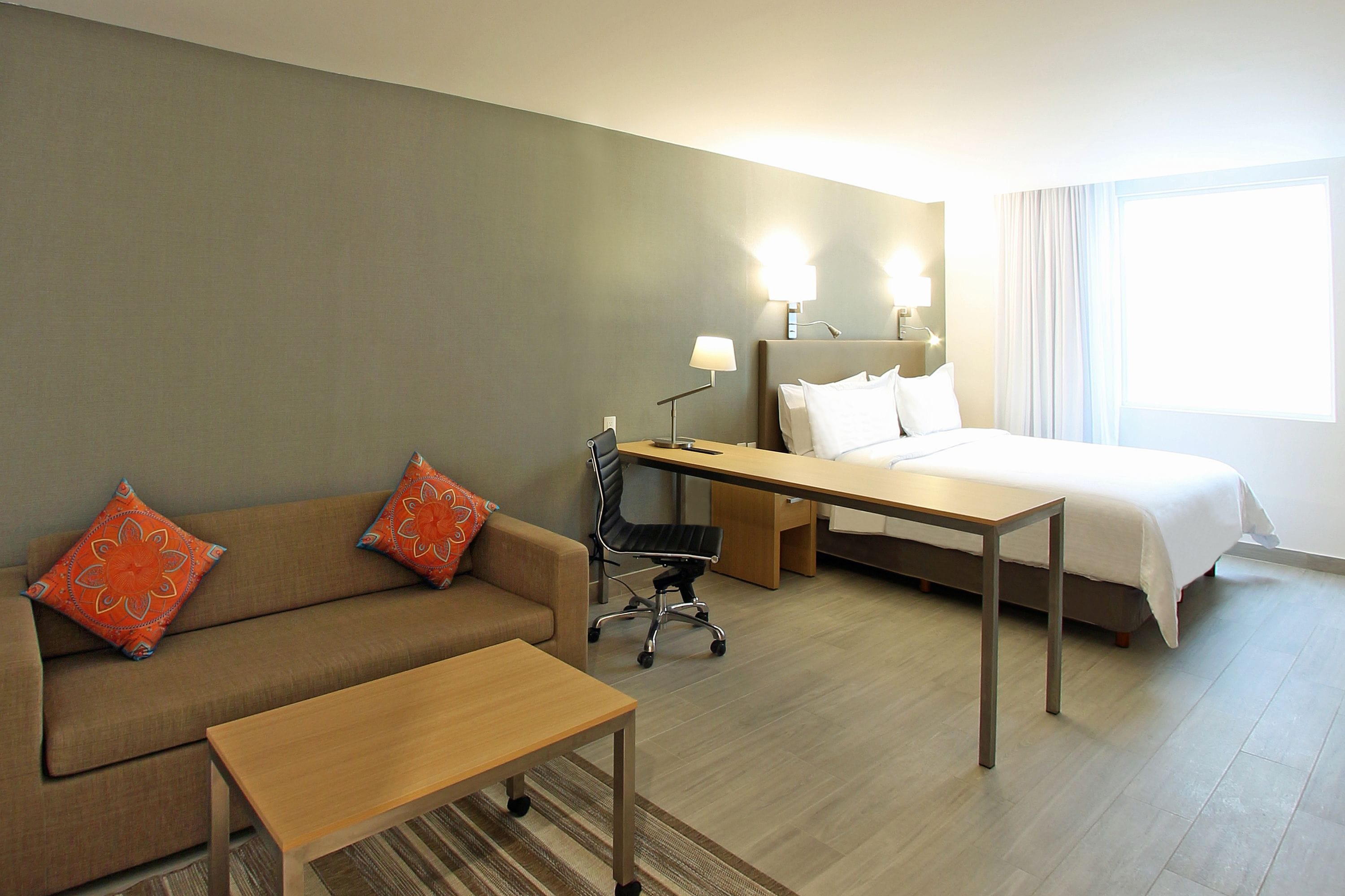 A hotel room with a bed, a desk, a chair, a sofa, and two lamps.