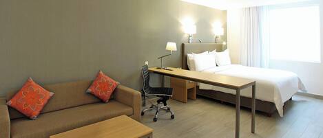 A hotel room with a bed, a desk, a chair, a sofa, and two lamps.