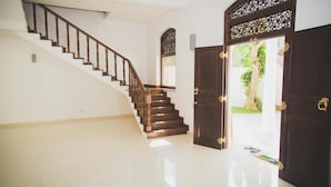 Una escalera con barandillas de madera que lleva a una plataforma, una puerta de madera oscura con un panel decorativo, y vistas de follaje en el exterior.