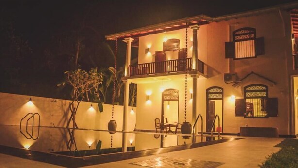 Un edificio de dos pisos con un balcón, una piscina y una entrada bien iluminada.