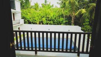 Vista desde un balcón con piscina, rodeado de exuberante vegetación y palmeras.