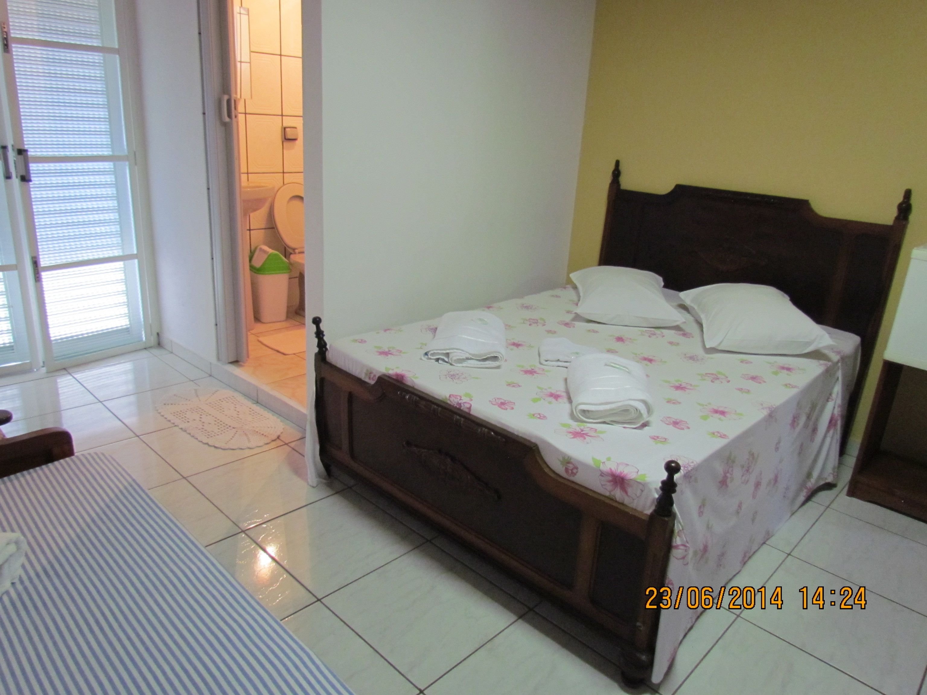 Une chambre à coucher avec un lit, une table de chevet, une lampe et une salle de bain visible à travers une porte ouverte.