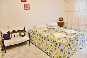 Ein Schlafzimmer mit einem Bett, das mit einem blumigen Bettbezug bezogen ist, einer Holzbank mit Kissen und einem kleinen Nachttisch mit einer Uhr und einer Vase.