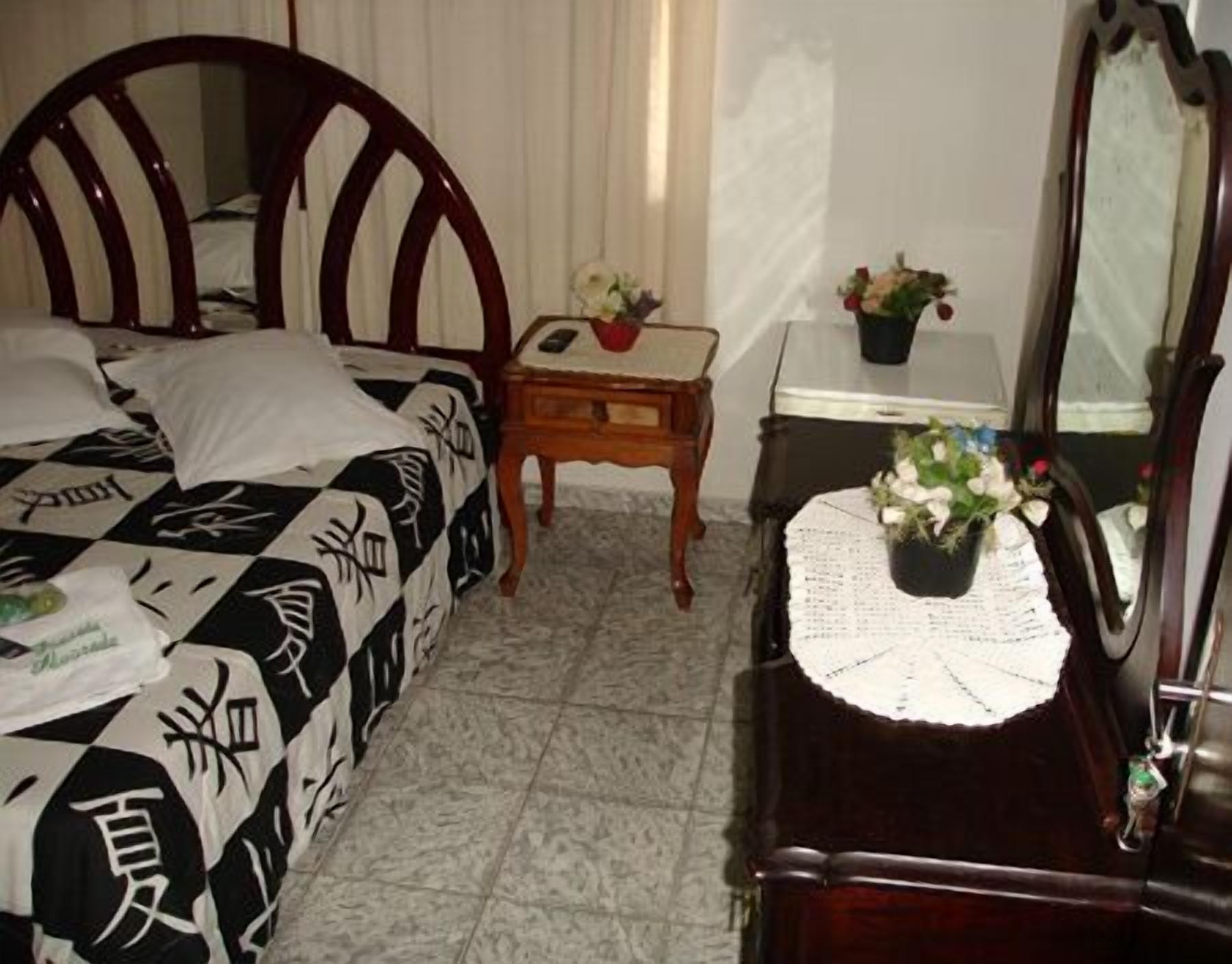 Un dormitorio con cama, mesita de noche con lámpara, cómoda y espejo.