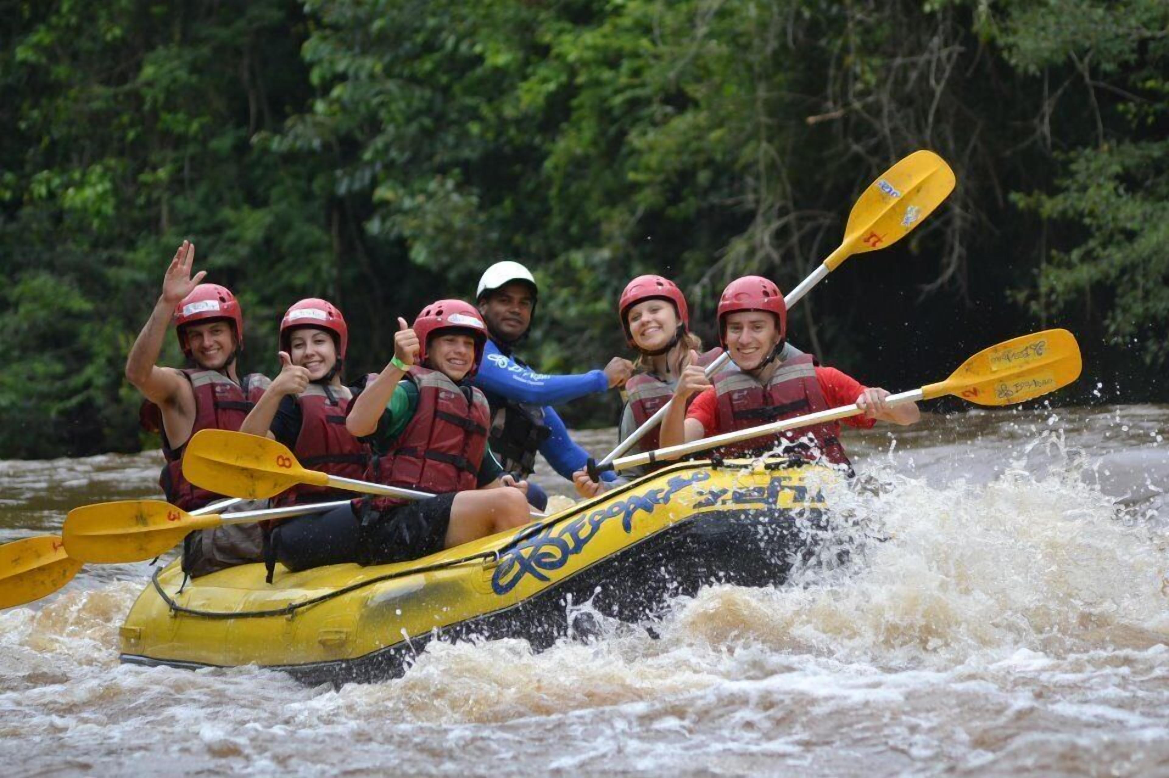 Eine Gruppe von Personen in einem gelben Raft mit Paddeln, die Helme und Schwimmwesten tragen und einen Fluss befahren.