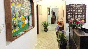 A hallway with a bulletin board displaying photos and notices, a calendar on the wall, and potted plants. - Hotel Pousada Alvorada (Brotas)