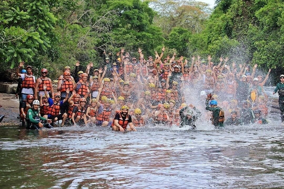 A group of people in a river, wearing life jackets and helmets, engaged in a water activity.