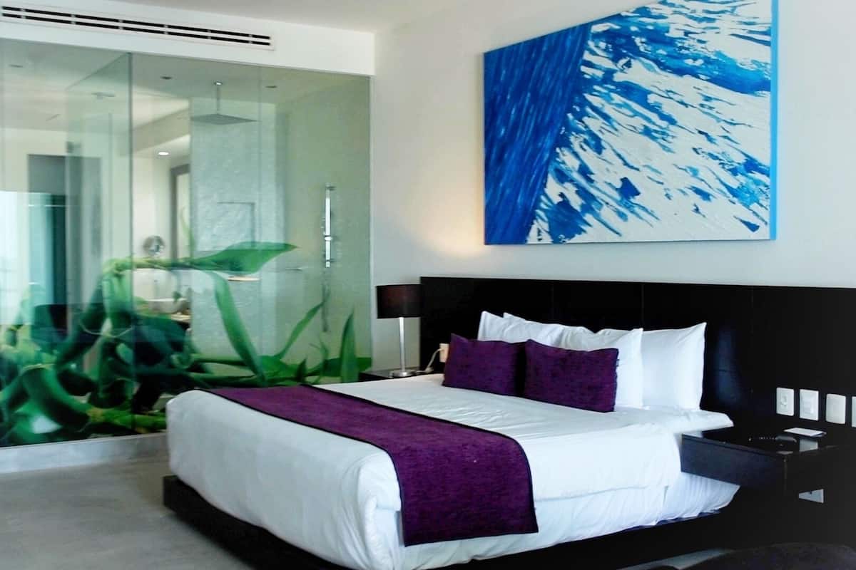 Ein modernes Hotelzimmer mit einem großen Bett, einer Glastrennwand und einem Gemälde einer blauen abstrakten Szene.