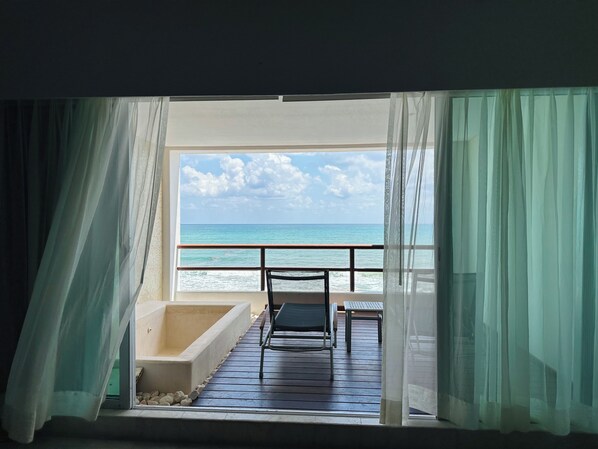 A balcony with a view of the ocean, a bathtub, and two chairs.