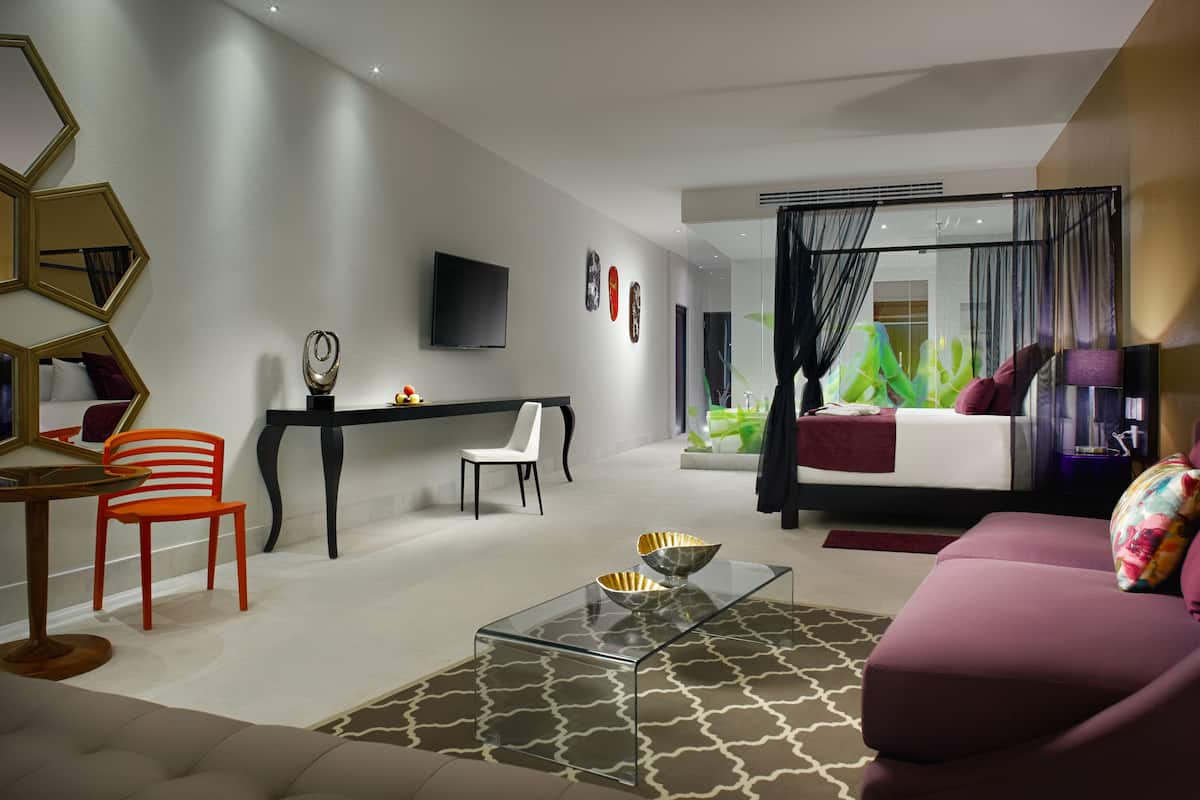 Ein modernes Wohnzimmer mit einem Glastisch, einer Couch, einem Esstisch mit Stühlen und einem an der Wand montierten Fernseher.