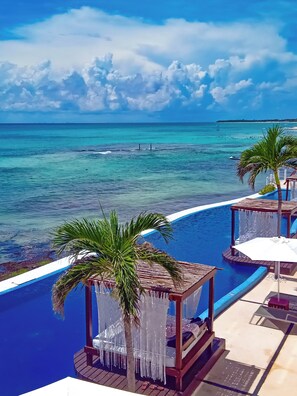 A poolside area with a view of the ocean, including a beach and a boat.