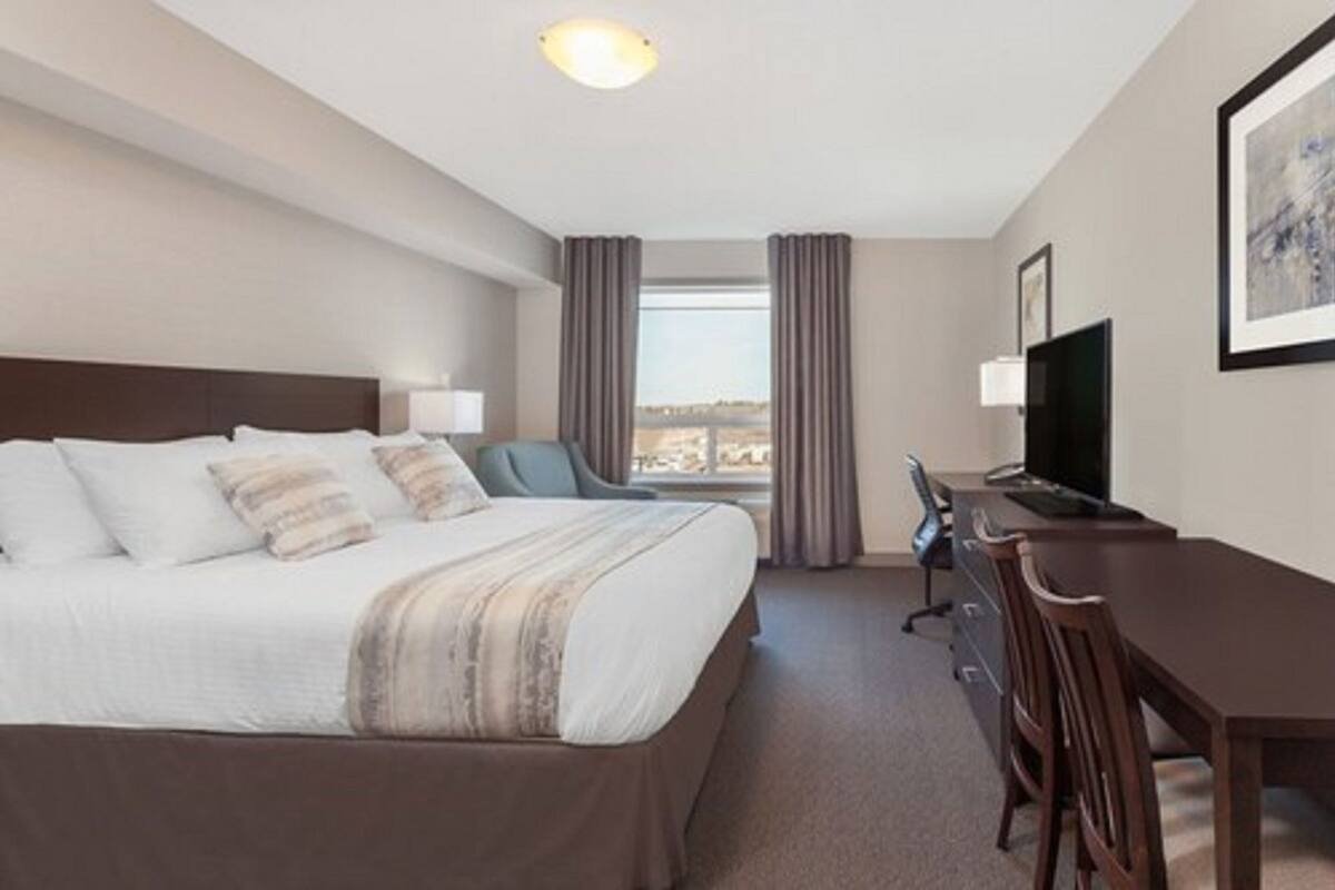 Habitación de hotel con cama, escritorio, silla, televisor y ventana con cortinas.