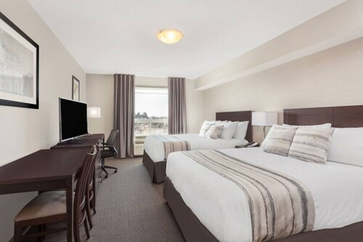 Una habitación de hotel con escritorio, dos camas, televisor y vista a la ciudad.