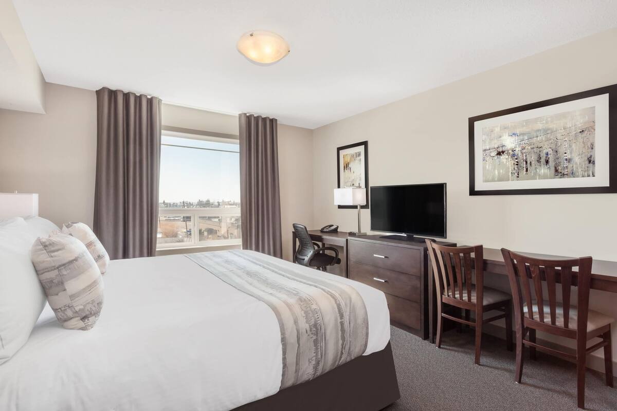 Habitación de hotel con una cama grande, un escritorio con silla, televisor y ventana con cortinas.