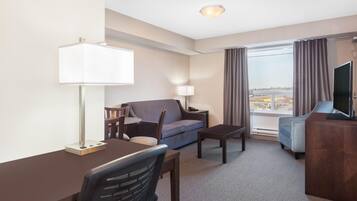 A hotel room with a desk, chair, sofa, TV, and a view of the outside.