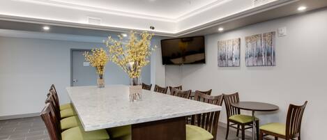 A modern dining area with a marble table, green cushioned chairs, and a flat-screen TV on the wall.