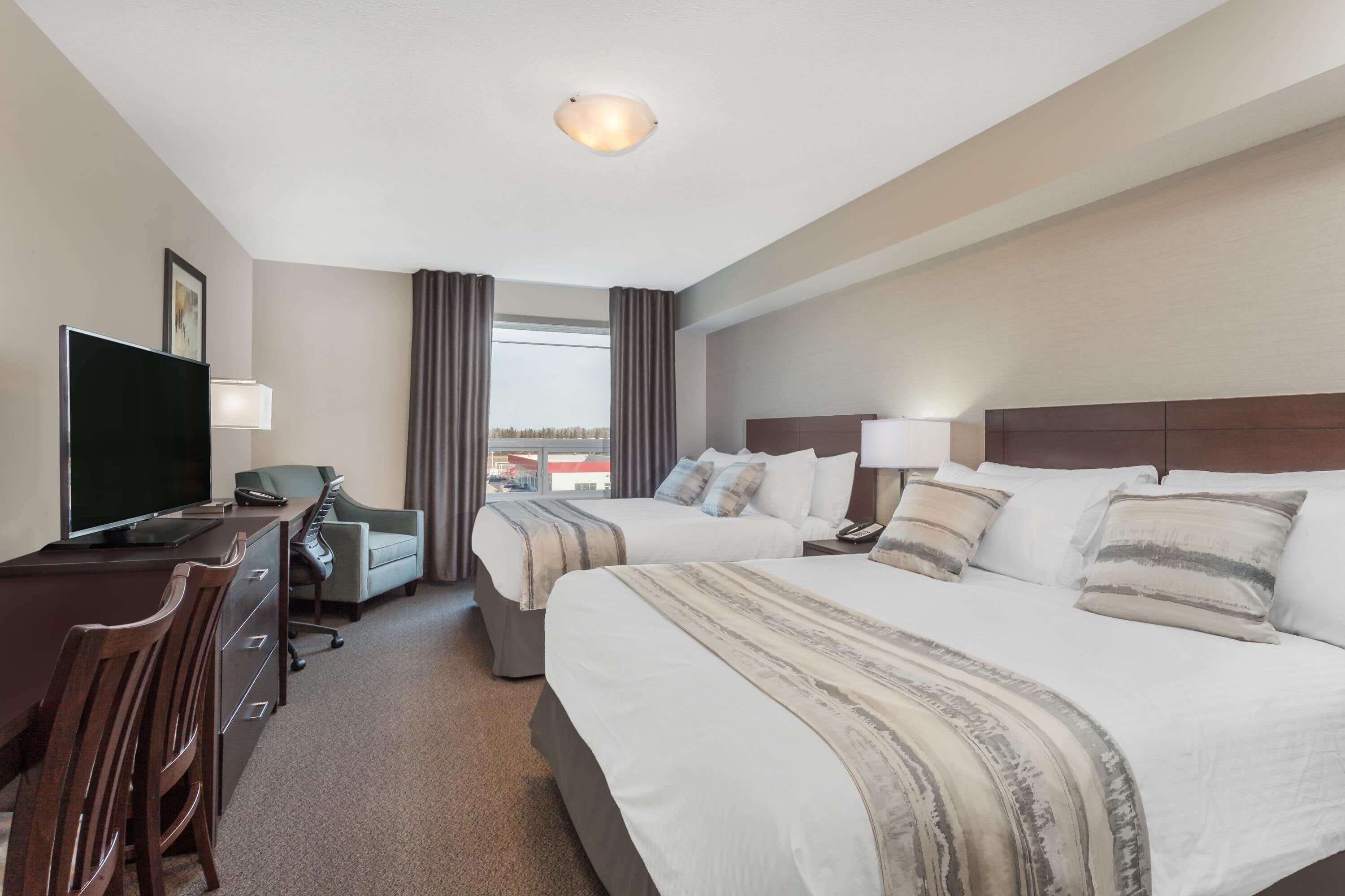 A hotel room with a desk, two beds, a TV, and a view of the outside.