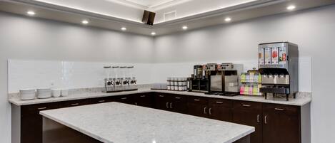 A modern kitchen with dark cabinetry, a large marble island, and a coffee machine.