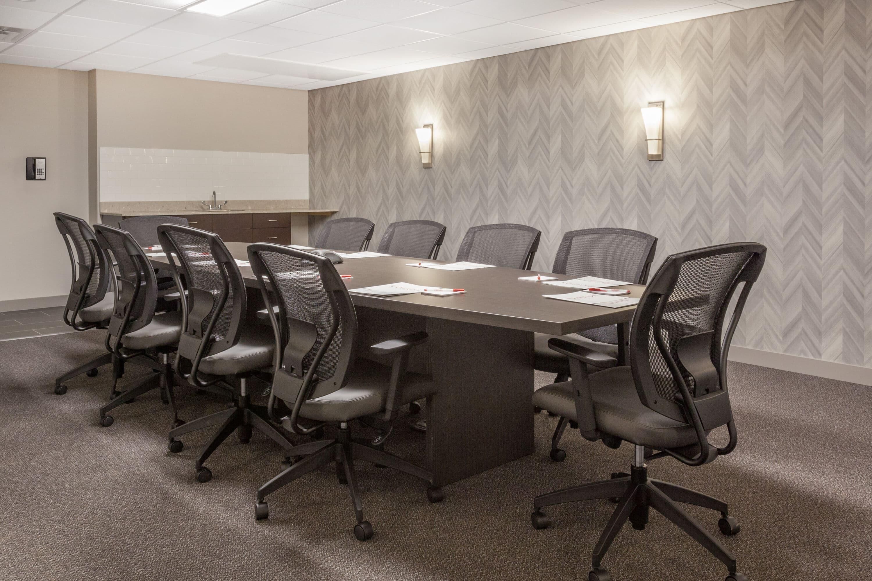 A conference room with a large table, eight chairs, a whiteboard, and two wall-mounted lights.