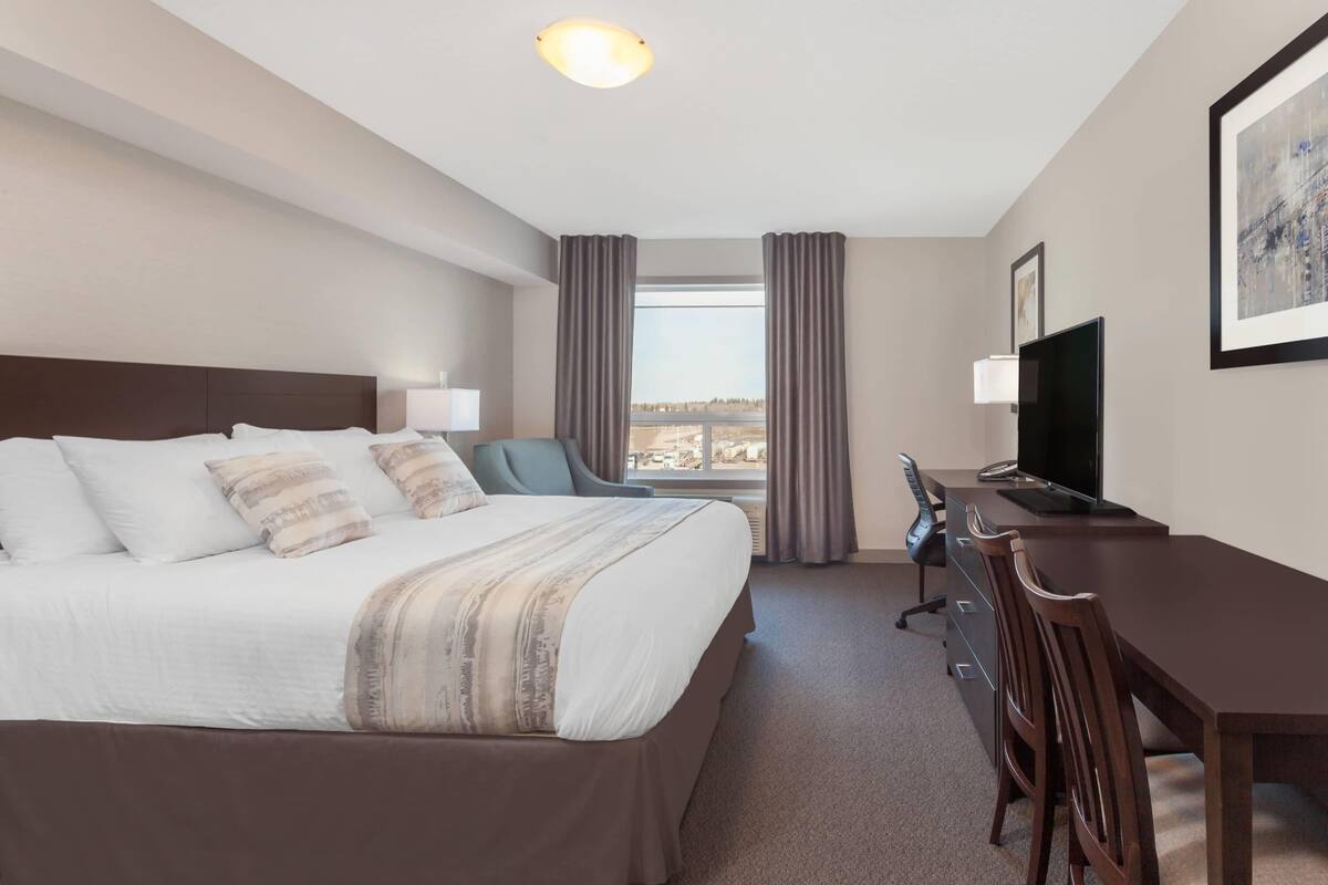 Una habitación de hotel con una cama grande, un escritorio, una silla, un televisor y una ventana con cortinas.