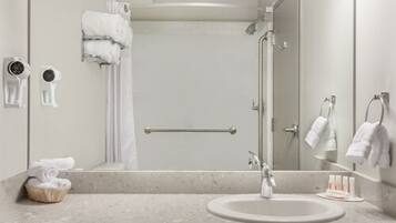 A modern bathroom with a large mirror, a sink, a shower with a handheld showerhead, and a towel rack.